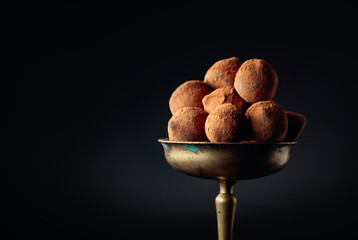 Chocolate truffles in old brass vase sprinkled with cocoa powder.