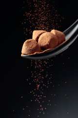 Chocolate candy truffle and flying cocoa powder on a dark background.
