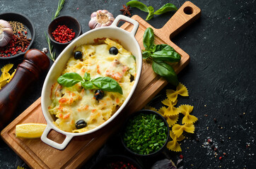 Baked farfalle pasta with salmon and cheese in a bowl on a black stone background. Top view. Rustic style.
