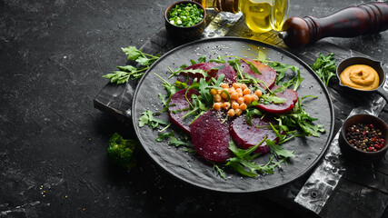 Vegan salad: beets, arugula and chickpeas on a black stone plate. Healthy diet food. Top view. Free space for text.