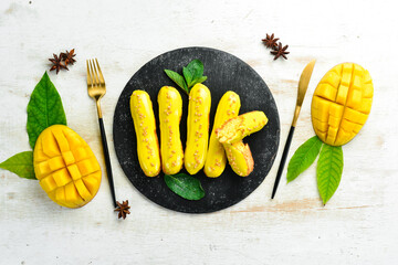 Eclair with mango cream. Mango dessert on a black stone plate. Top view. Rustic style.