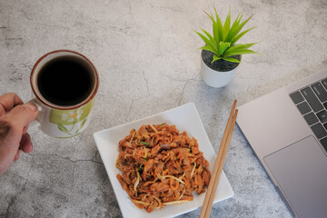 Man hand hold a cup of coffee over healthy breakfast concept on work table background with laptop  in home office.