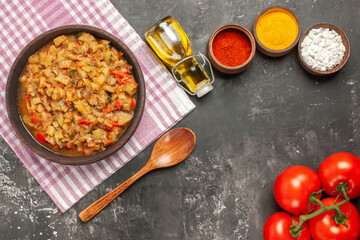 top view roasted eggplant salad in bowl oil wooden spoon tomatoes on dark background
