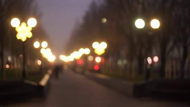 Blurry sity sidewalk in park with glowing lights and rows of bare trees.