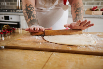 Closeup of man's hands rolling dough with pin. Working with pastry or bakery cooking.