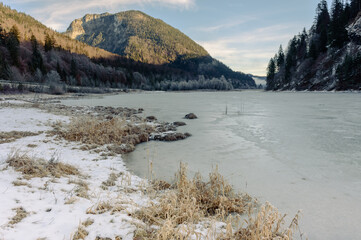 Gefrorener See in den Bergen mit Wald, Schatten und Sonnenlicht