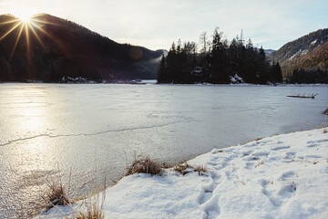 Sonne spiegelt  sich im Eis des Sees in den bergen im Winter mit Wald und Himmel