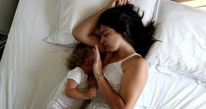 Mother cuddling and breastfeeding infant baby one year old toddler in bed