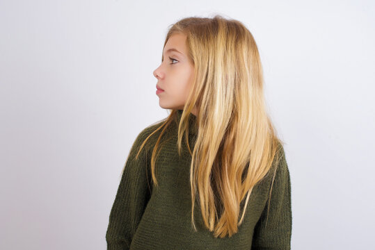 Close up side profile photo Caucasian kid girl wearing green knitted sweater against white wall 
 not smiling attentive listen concentrated