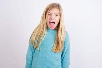 Cute Caucasian kid girl wearing blue knitted sweater against white wall with happy and funny face...