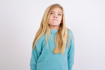 Cute Caucasian kid girl wearing blue knitted sweater against white wall with snobbish expression curving lips and raising eyebrows, looking with doubtful and skeptical expression, suspect and doubt.