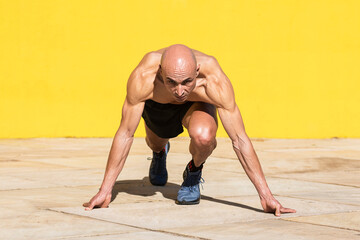 Man with starting position for a race in front of a yellow wall