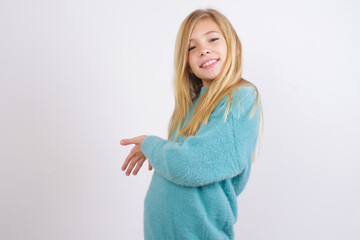 Cute Caucasian kid girl wearing blue knitted sweater against white wall Inviting to enter smiling natural with open hands. Welcome sign.