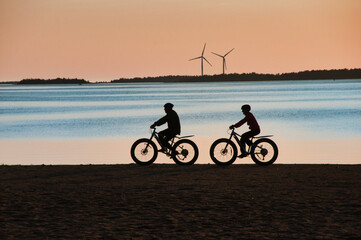 Fototapeta premium Two persons biking on the beach in warm sunset.