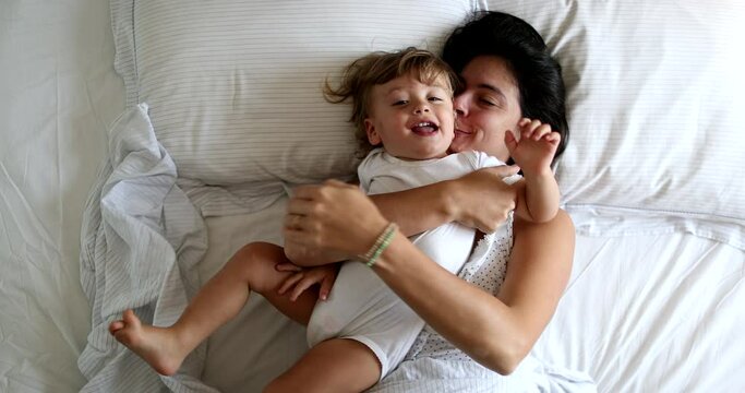Mother cuddling with baby toddler boy in bed in the morning