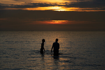 Silhouette couple standing midth of sea in the warm light evening time