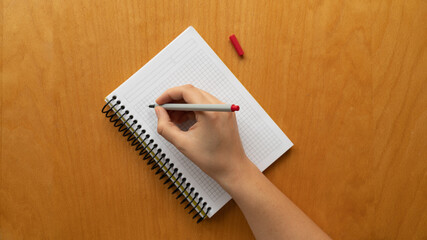 Taking notes in blank paper white notebook. graph, grid, black squared, woman hand and red pencil on wooden table background. new year's resolution, goals. 2021. coronavirus. 