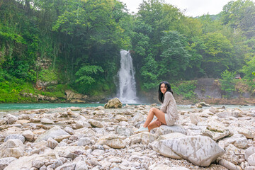 female tourists sits on the rock with Martvili waterfall and river in the backgroundc