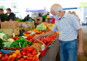 retired european man wearing medical mask protecting against virus buying tomatoes in market