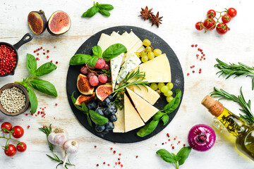 Assorted cheeses on a plate. Parmesan cheese, blue cheese and brie on a plate with grapes and figs. Antipasto. Top view. - obrazy, fototapety, plakaty