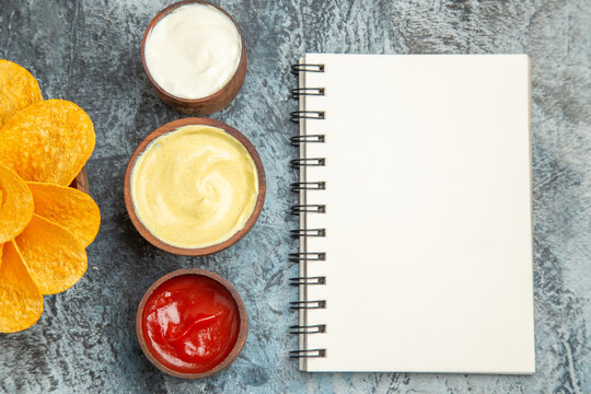 Homemade potato chips decorated like flower shaped and salt with ketchup mayonnaise and notebook on gray background