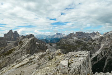 Fototapeta na wymiar An endless view on a high and desolated mountain peaks in Italian Dolomites. The lower parts of the mountains are overgrown with moss and grass. Raw and unspoiled landscape. Few clouds above the peaks