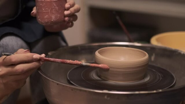 The process of making tableware from natural clay on a potter's machine, the hand paints the bowl with a brush with clay paint   
