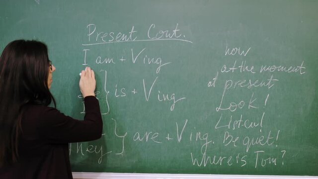 Online schooling. teacher is explaining material during online English lesson. She is writing grammar rules with chalk on blackboard, in school class. remote teaching. live video streaming from class.