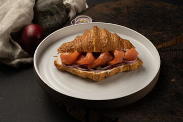Croissant with salmon, ricotta, capers and pickled onions. Light breakfast of pastries, fish and vegetables.