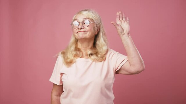Skeptical elderly woman showing Bla bla gesture with her hand, expressing mistrust and disbelief, pink background
