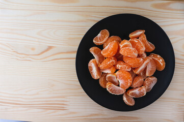 Tangerine slices on a black plate on a wooden background