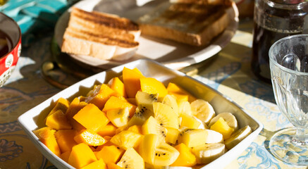Large plate of fresh exotic fruits for breakfast, mango, bananas, golden kiwi on a table with toasted bread