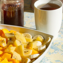 Large plate of fresh exotic fruits for breakfast, mango, bananas, golden kiwi on a table with tea and strawberry jam