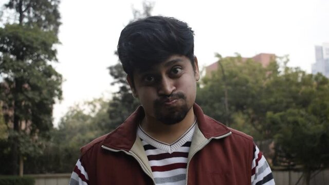 Indian boy making funny faces by puffing his mouth and cheeks with air and moving his head. He is wearing stripped Shirt   