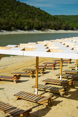 Wooden sun loungers and beach umbrellas on a sandy lakeshore in Sukko, Russia on a hot summer day