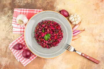 top view of bowl of a red salad with greens on it on a wooden backgorund with vegetables at the side with checked napkin with fork on it