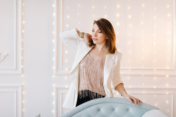 Attractive young woman in a business suit with white jacket, black pants and high heels near a blue classic sofa. White background with light