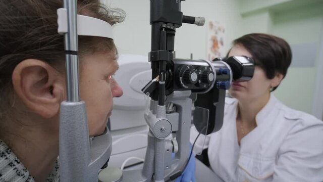 Woman doctor is viewing through ophthalmoscope in eyes of patient in ophthalmologic clinic. Professional inspection of vision