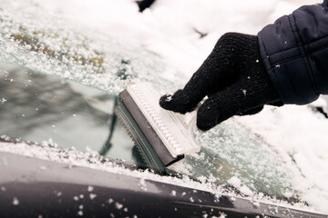 A male driver cleans ice and snow off the car windscreen with a scraper