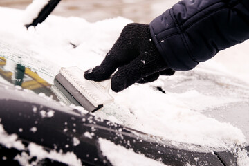 A male driver cleans ice and snow off the car windscreen with a scraper