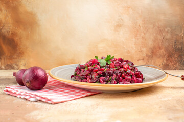 side view of plate of a red salad with greens on it on a wooden backgorund with vegetables at the side with a fork on it with checked napkin