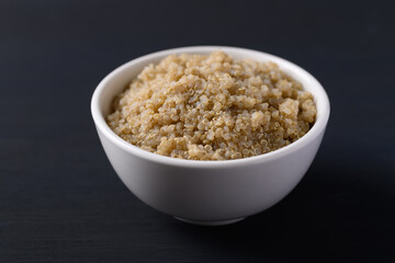 Cooked brown quinoa seeds in a bowl on black background, Healthy vegan food