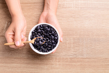 Black kidney beans in a bowl holding by hand with spoon on wooden background, Top view