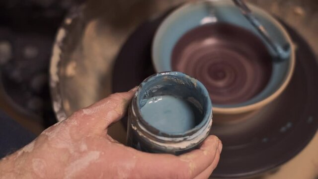 The process of making tableware from natural clay on a potter's machine, the hand paints the bowl with a brush with clay paint   