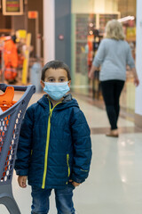 Boy wears protected mask in store. Shopping time during coronavirus outbreak. Boy in a medical mask. Shopping with kids during virus outbreak. Boy in face mask in supermarket
