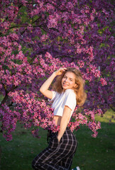 beautiful cheerful happy teenager girl near blooming pink spring tree. Smiles, enjoys the moment. Romance, harmony, relaxation. Hi spring