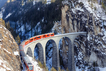 Luftaufnahme eines roten Zuges, der das Landwasserviadukt in den Schweizer Alpen überquert