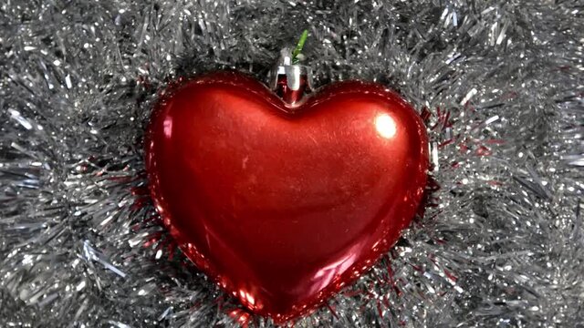 Close-up of a Christmas tree toy in the form of a heart lies on the New Year's silver tinsel and slowly moves clockwise. Christmas winter background. Happy New Year.