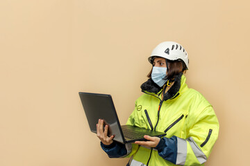 Female industrial worker in medical mask. Woman engineer with white hard hat helmet working on laptop computer. Climber