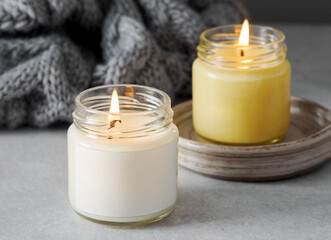 Burning candles on grey table, space for text. Grey knitted scarf and scented candles. Cozy winter atmosphere. 2021. Сolors of the year. burning candles on a gray background. New Year. Romantic.